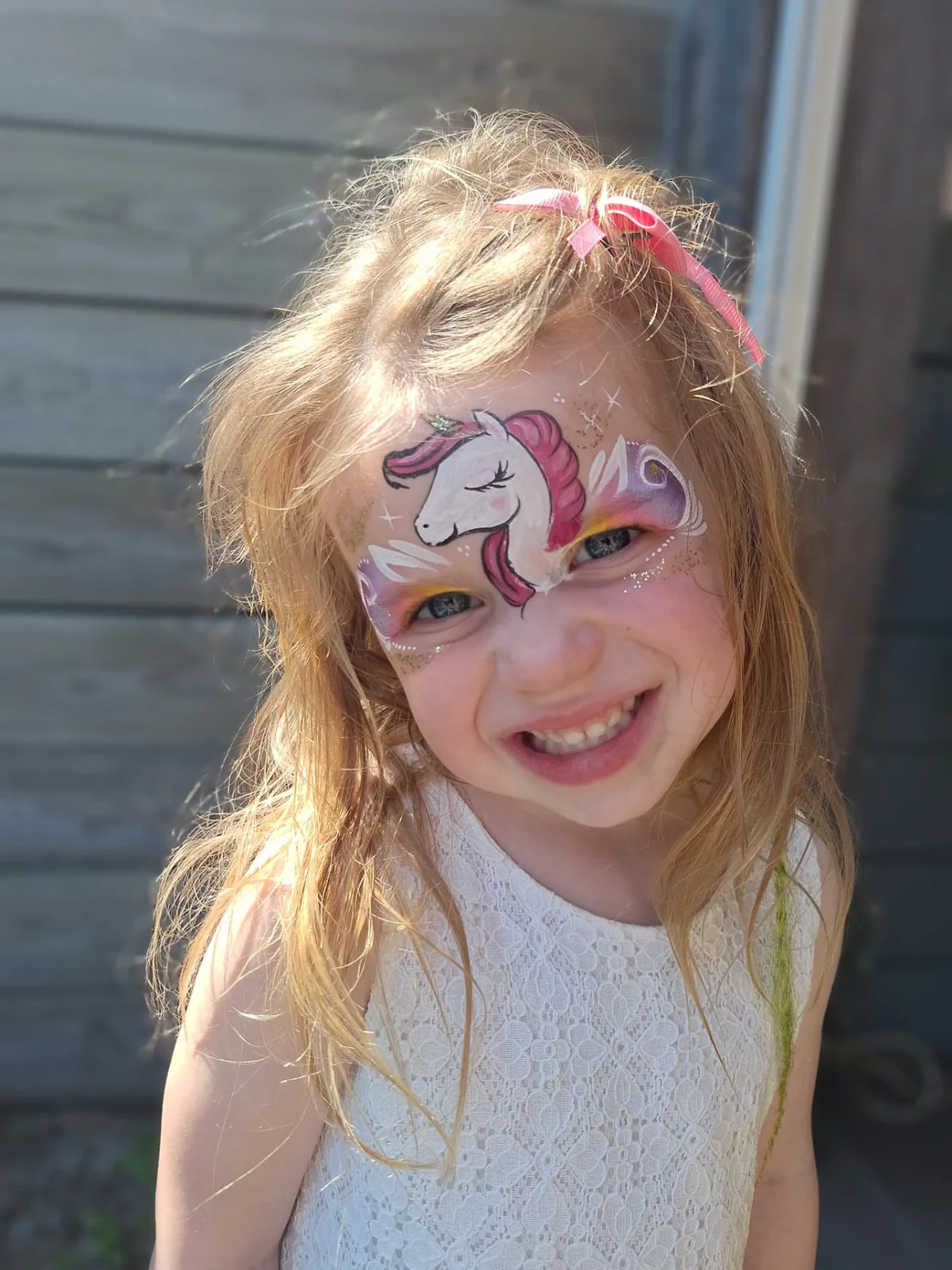 Lachend kind met een roze eenhoorn geschminkt op het gezicht
